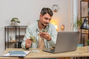 persona contando billetes frente a computadora